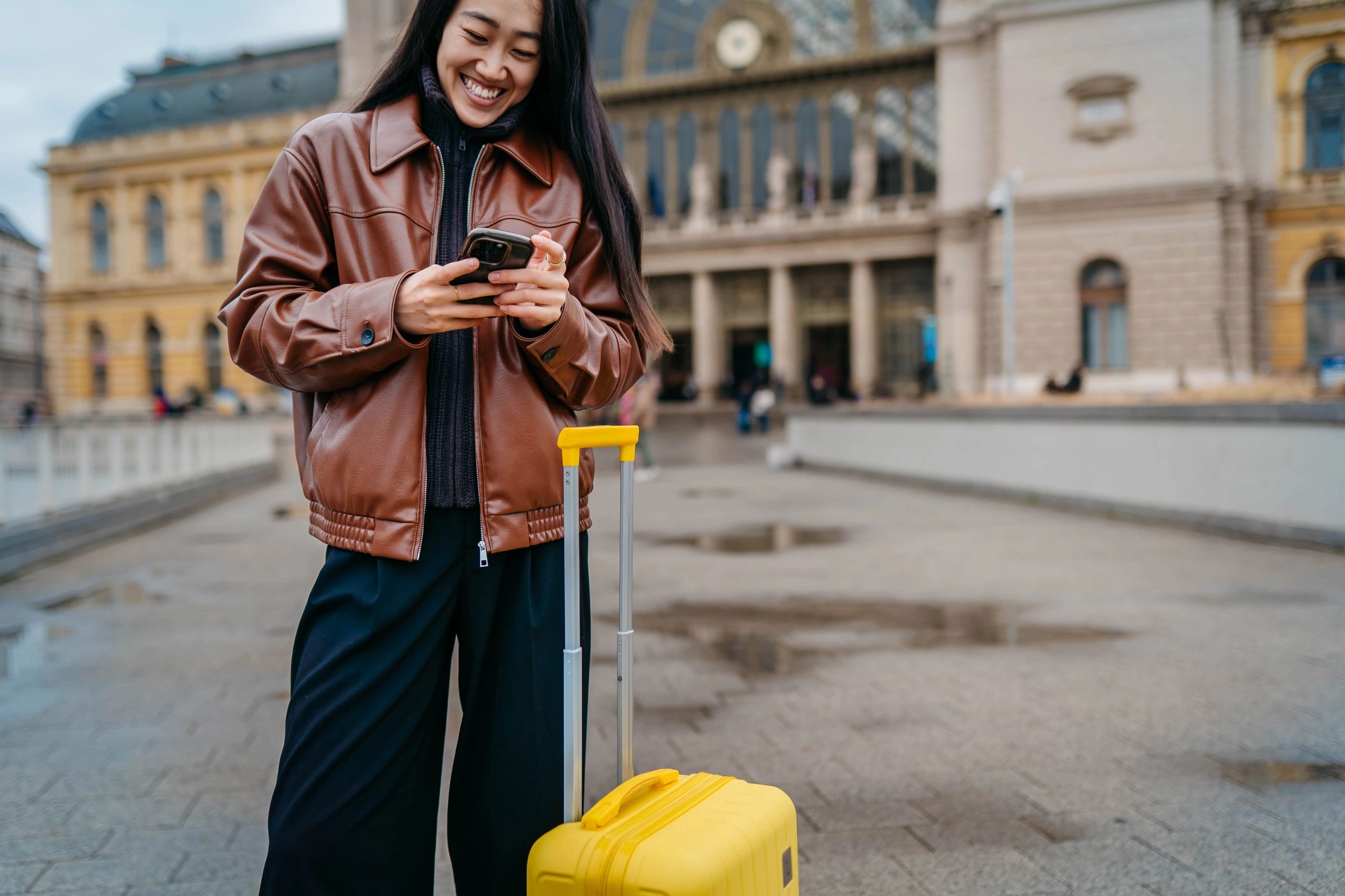 Young traveler with suitcase using a smartphone outdoors